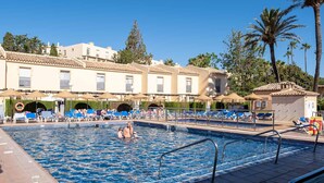 Een zwembadgedeelte met ligbedden en parasols, omringd door gebouwen in mediterrane stijl.