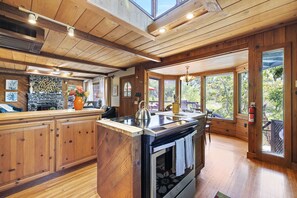 A spacious kitchen with wooden cabinetry, a central island with a stove, and large windows offering views of the outdoors. - River Frontage ~ Quiet & Secluded Retreat Only Minutes to Sequoia National Park (Three Rivers)