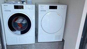 Dos lavadoras Miele blancas en un lavadero pequeño con suelo de baldosas grises.