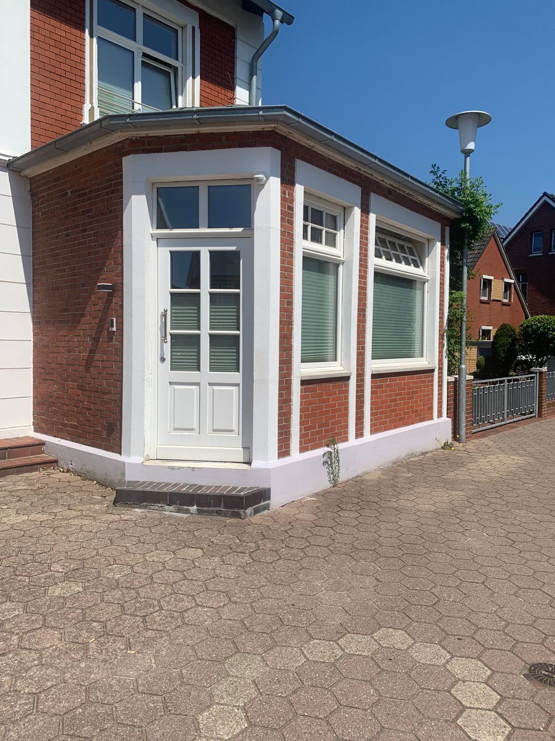 Une maison d’angle avec une porte blanche, deux fenêtres avec des volets et un petit porche.