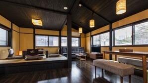 A modern interior with dark wooden floors, a black leather sofa, a wooden table, and a bench. Large windows provide natural light and views of the outside. - Tofukuji SAKURA (Kyoto)