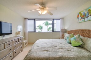 Quarto com cama, ventoinha no teto, televisão, cómoda, janela com persianas e um quadro.