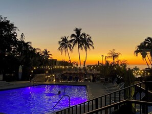 A swimming pool with a person swimming, surrounded by palm trees and a sunset view. - Moon Bay Condo, Paradise Found! Heated pool/marina (Key Largo)