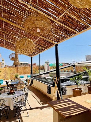 Relax in a shaded patio area with a round table and comfortable seating, surrounded by lush greenery and a scenic view.