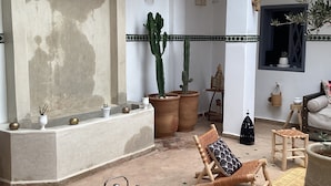 A spacious interior with a high ceiling, a large arched doorway, and a seating area with a woven chair and cushions. - Charming morrocan Riad & Spa in Marrakech (MARRAKECH)