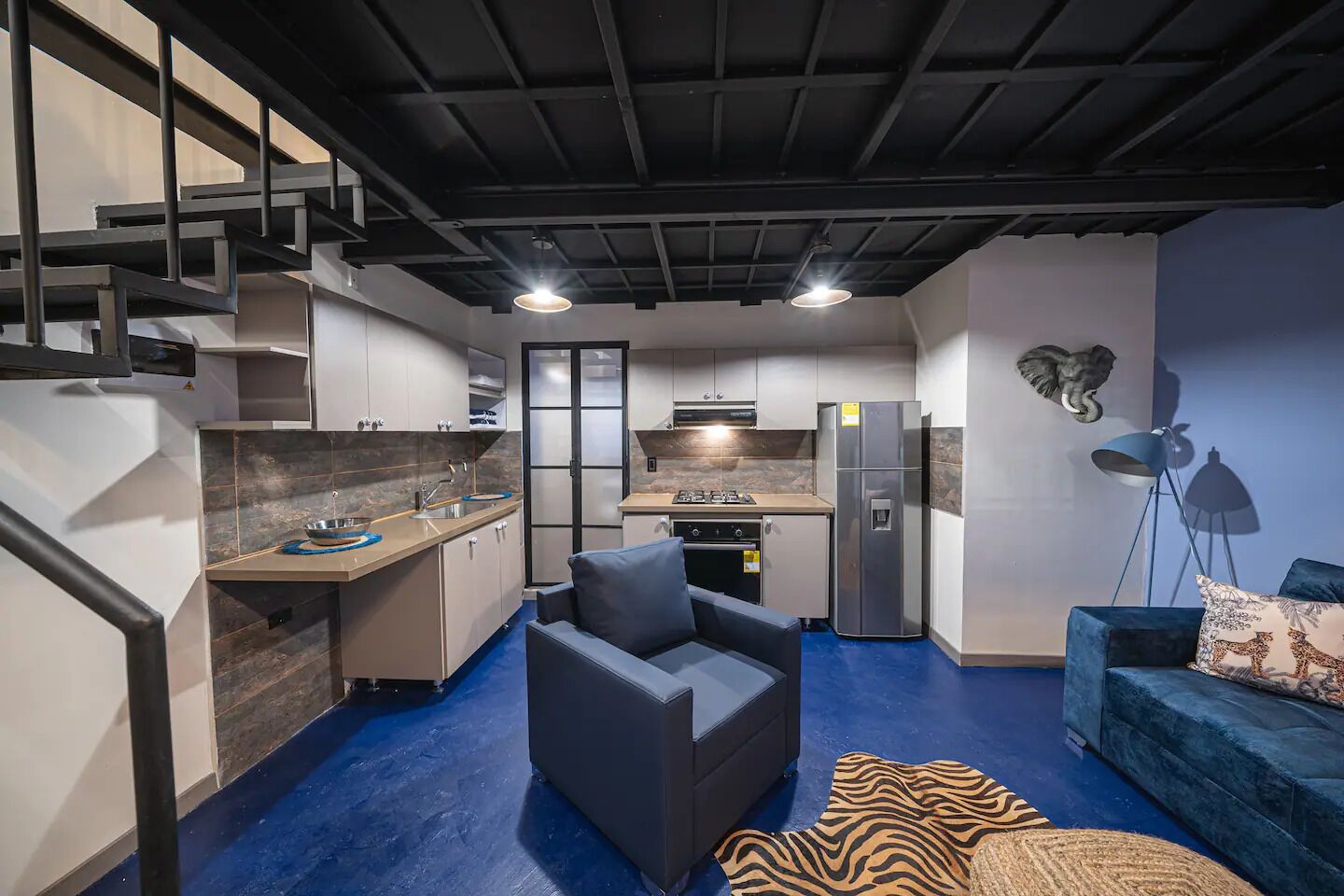A compact living space with a kitchen, a sofa, and a staircase.