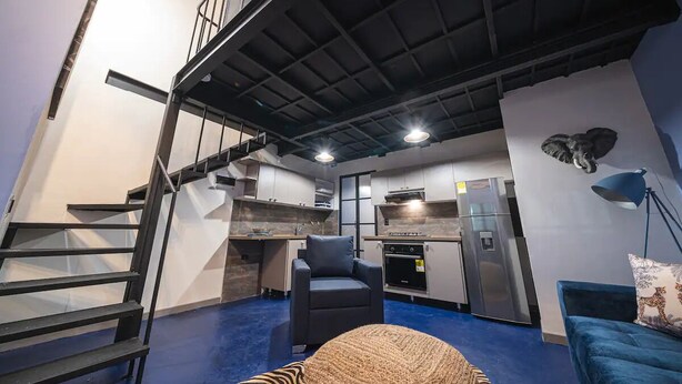Un intérieur moderne comprenant un escalier, une cuisine, un coin salon et un plafond avec des poutres apparentes.