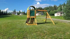 Un ensemble de balançoires en bois installé dans un champ d’herbe, avec des maisons en arrière-plan.