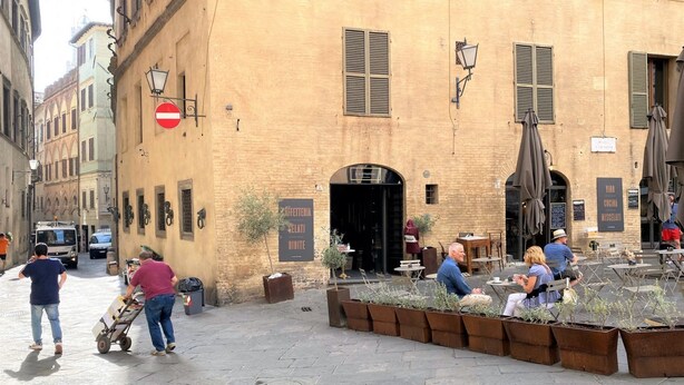 A street with outdoor seating, a building with a sign for a gelateria, and a no entry sign. - PALAZZETTO SAN GIOVANNI-in front of the Baptistry (Siena)