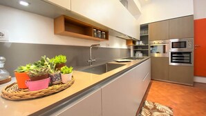 A modern kitchen with a central island, built-in appliances, and a wooden shelf above the sink. - PALAZZETTO SAN GIOVANNI-in front of the Baptistry (Siena)