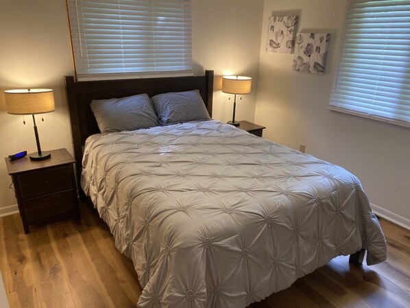Una cama bien hecha con un edredón capitonado, dos lámparas de noche, una mesita de noche con un reloj digital y una pared decorada con motivos florales.