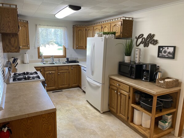 A modern kitchen with wooden cabinets, a white refrigerator, a microwave, and a coffee machine. - Cute & Cozy 2 Bedroom Home (Negaunee)