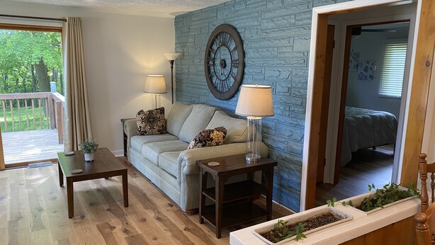 Una sala de estar con un sofá, dos lámparas, un reloj y vistas a un dormitorio.