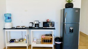 Una kitchenette compacta con dispensador de agua, cafetera, microondas y refrigerador.