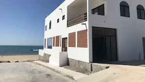 Un edificio moderno de dos pisos con balcón, entrada protegida por una reja y vista al mar.