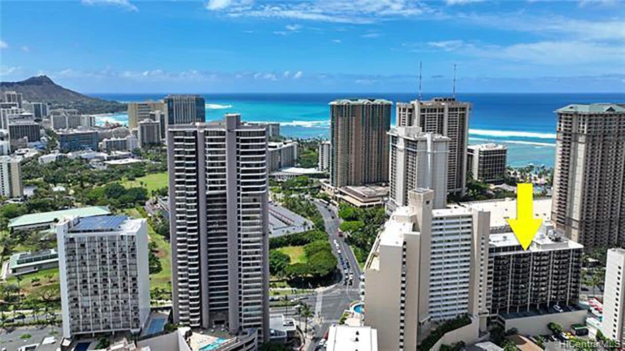 A high-rise hotel with multiple floors, surrounded by greenery and a view of the ocean.
