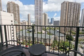 A balcony with wicker chairs and a view of high-rise buildings and a parking area. - Fully modernized 11th floor studio at The Palms (Honolulu)