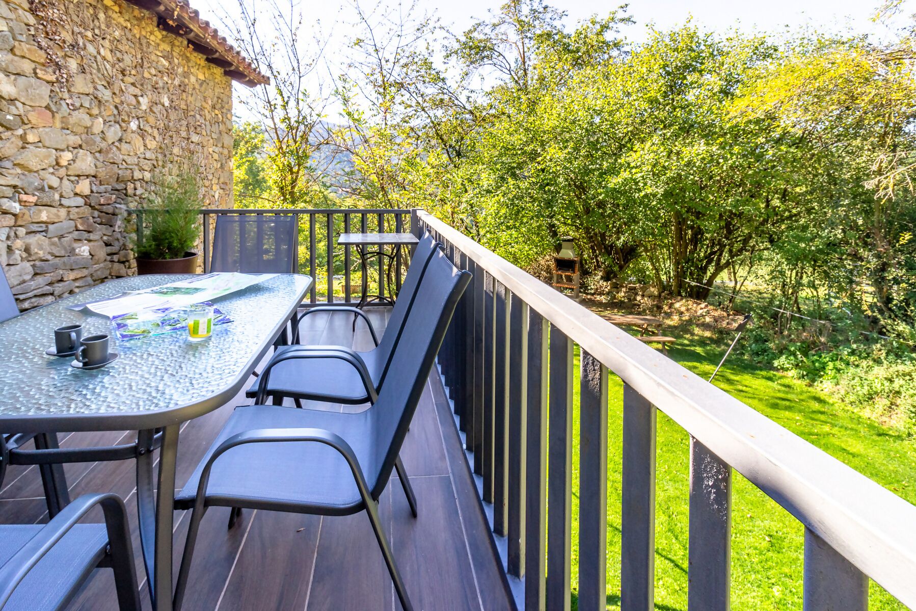 A patio with a table and chairs, a stone wall, and a view of greenery.