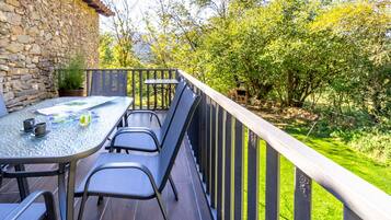 A patio with a table and chairs, a stone wall, and a view of greenery.