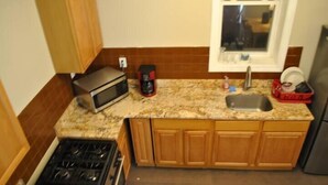 A kitchen with wooden cabinets, a granite countertop, a microwave, a coffee maker, a sink, and a dish rack. - Motel Casa Downtown Guest House (Newark)