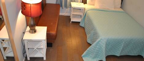 Un dormitorio con cama, una mesita de noche con lámpara, un banco de madera y un espejo.