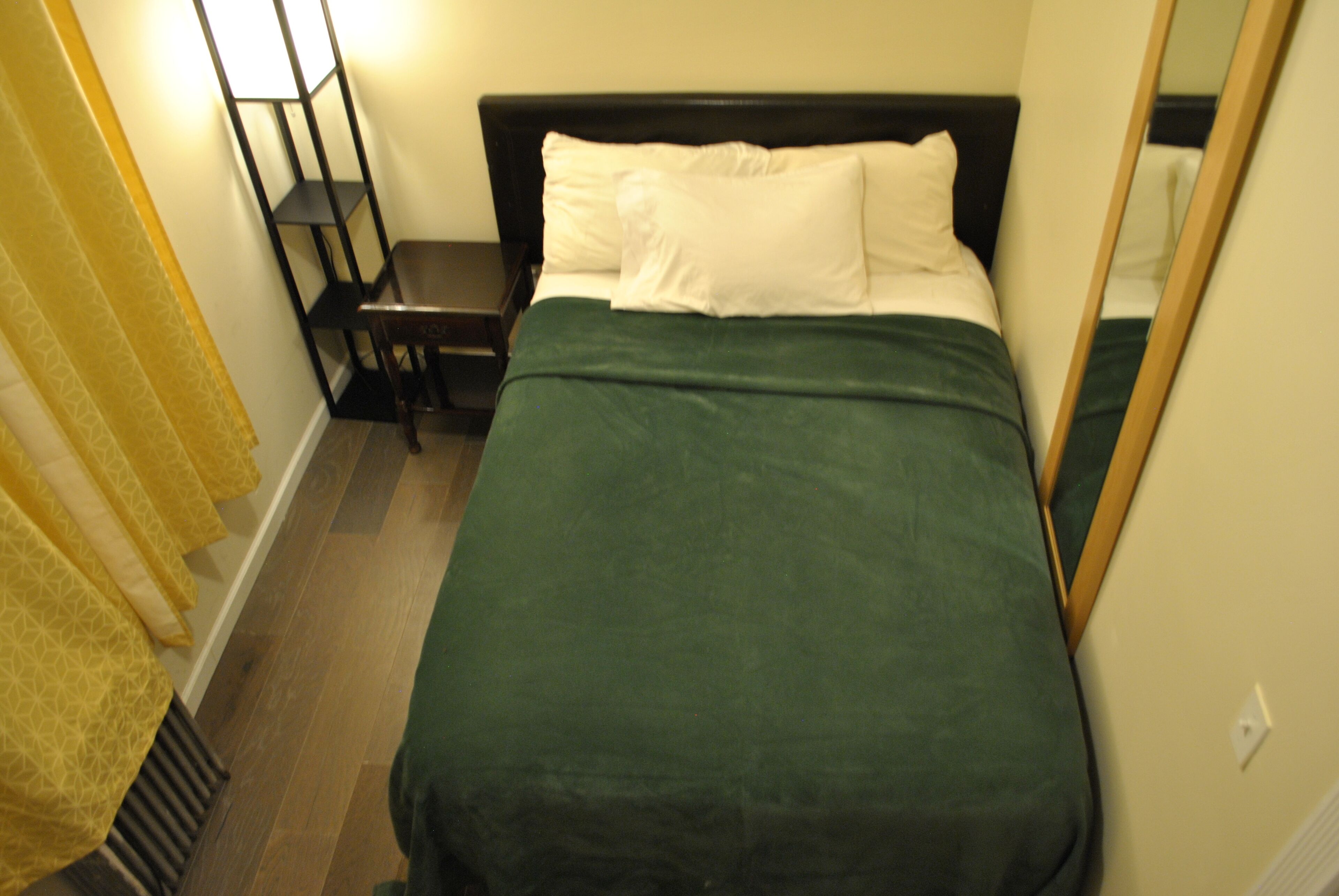 A hotel room with a bed, a nightstand, a mirror, and a yellow curtain.