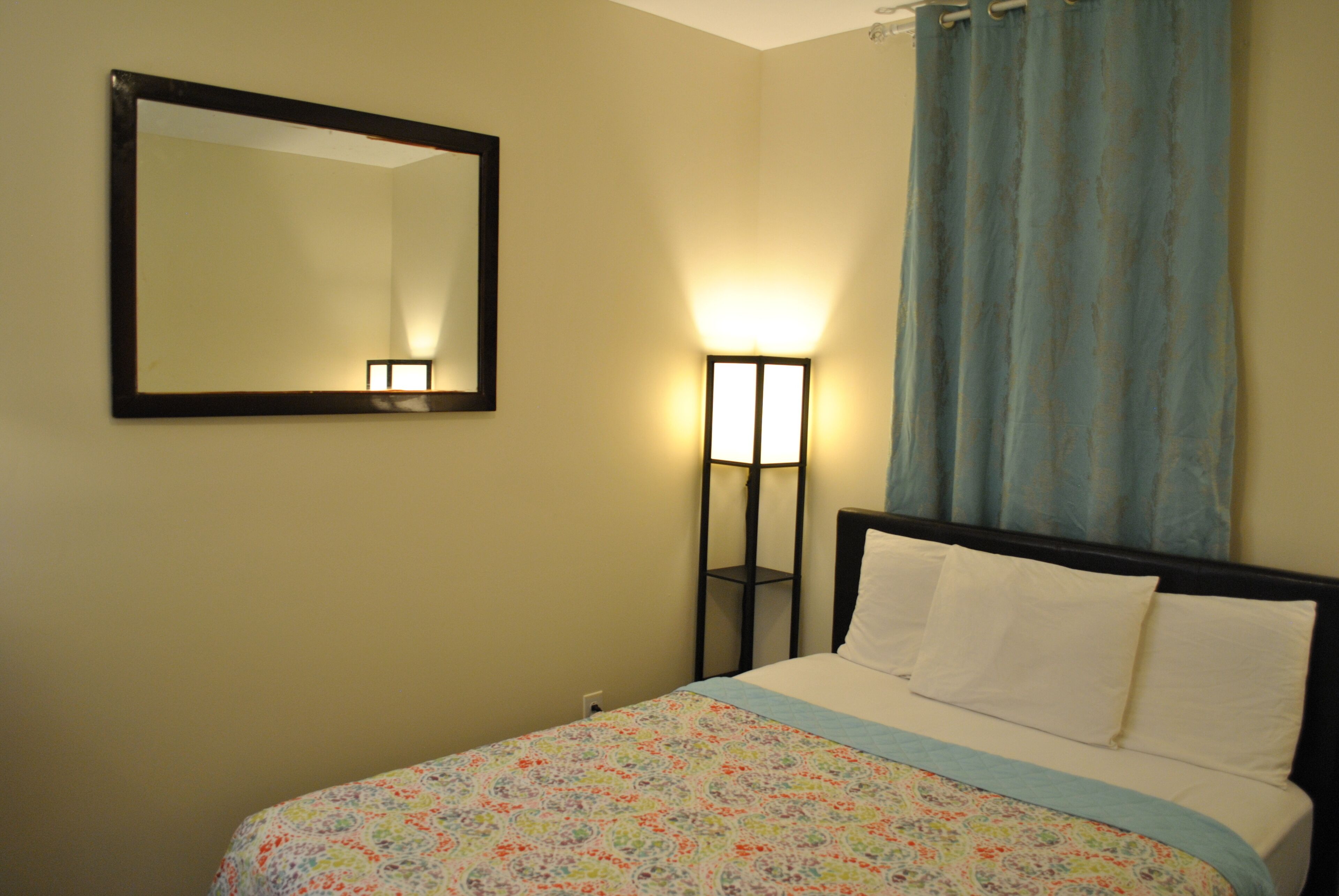 A bedroom with a bed, a nightstand, a mirror, and a floor lamp.