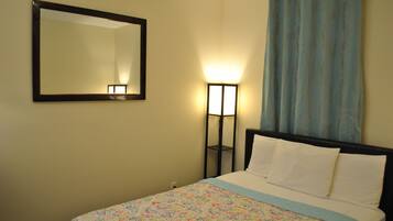 A bedroom with a bed, a nightstand, a mirror, and a floor lamp.