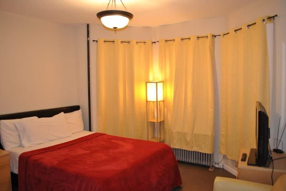 A hotel room with a bed, a lamp, a television, and curtains.
