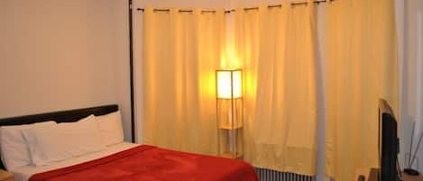 A hotel room with a bed, a lamp, a television, and curtains.