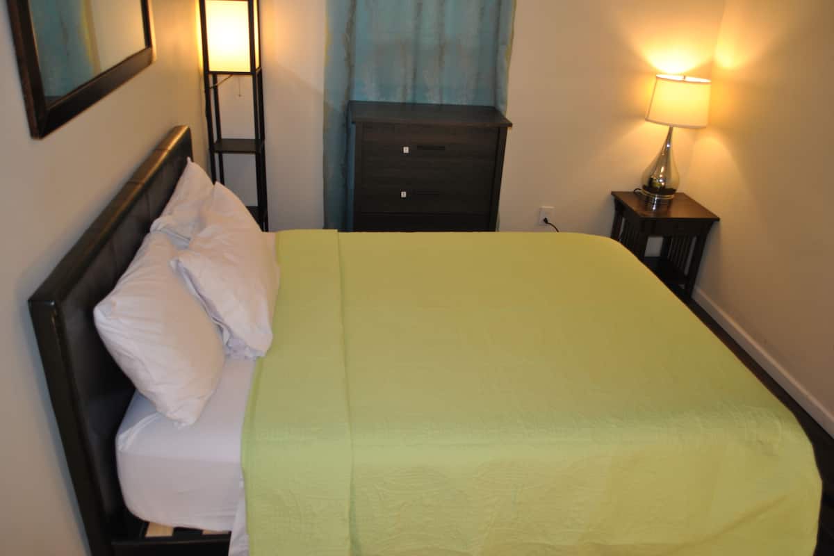 A neatly made bed with white pillows and a green bedspread in a hotel room.