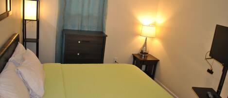 Una habitación de hotel con cama, mesita de noche, lámpara y televisión.
