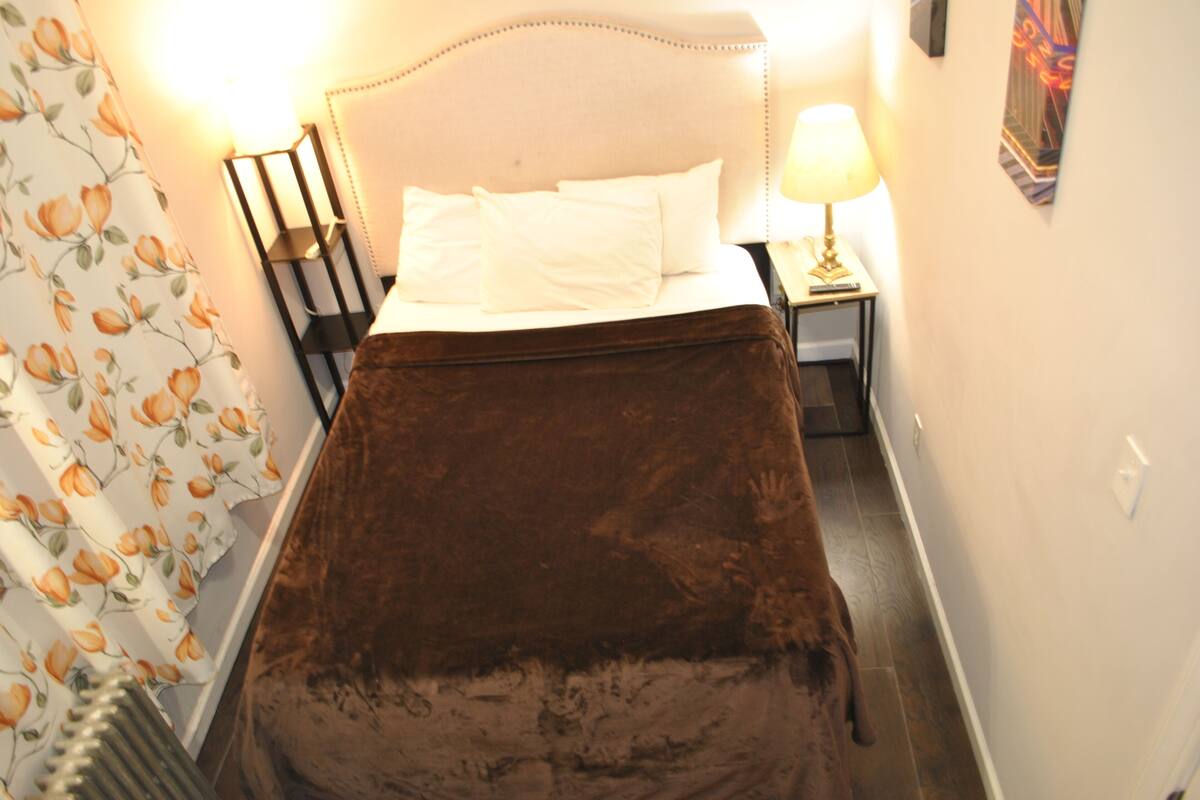 A bedroom with a bed, a nightstand, a lamp, and a wall-mounted artwork.