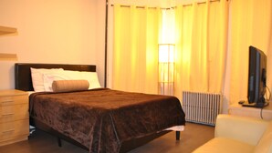 A hotel room with a bed, a bedside table, a lamp, a chair, and a television. - Motel Casa Downtown Guest House (Newark)