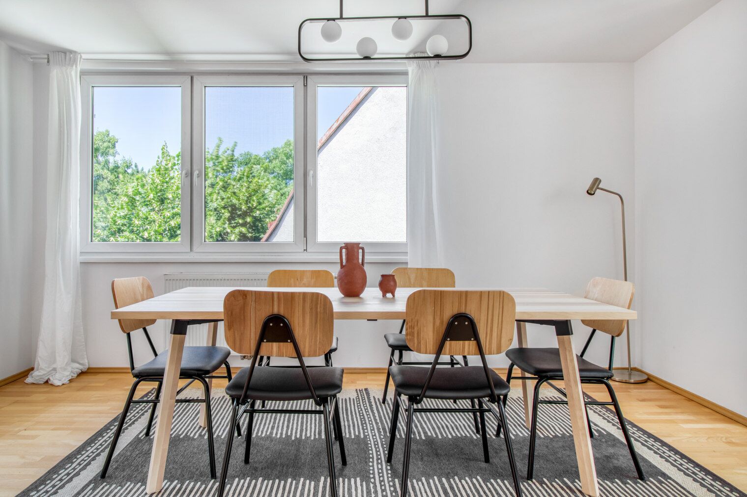 Een eethoek met een tafel en stoelen, grote ramen en uitzicht op groen buiten.