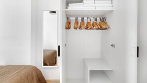 Un dormitorio minimalista con cama, armario con ropa colgada y espejo.