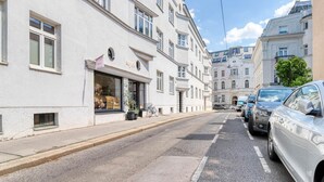 Una calle con coches aparcados y un edificio con una tienda en la planta baja.