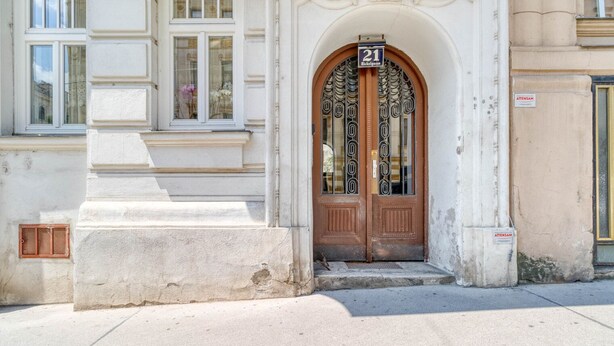 Une entrée d’immeuble avec une grande porte en arc de cercle, une plaque indiquant le numéro de l’immeuble et une petite marche menant à la porte.