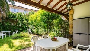 Un patio al aire libre con una mesa redonda y sillas, rodeado de follaje y un muro de piedra.