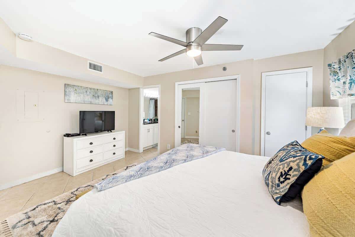 A bedroom with a bed, a ceiling fan, a TV on a dresser, and a door leading to another room.
