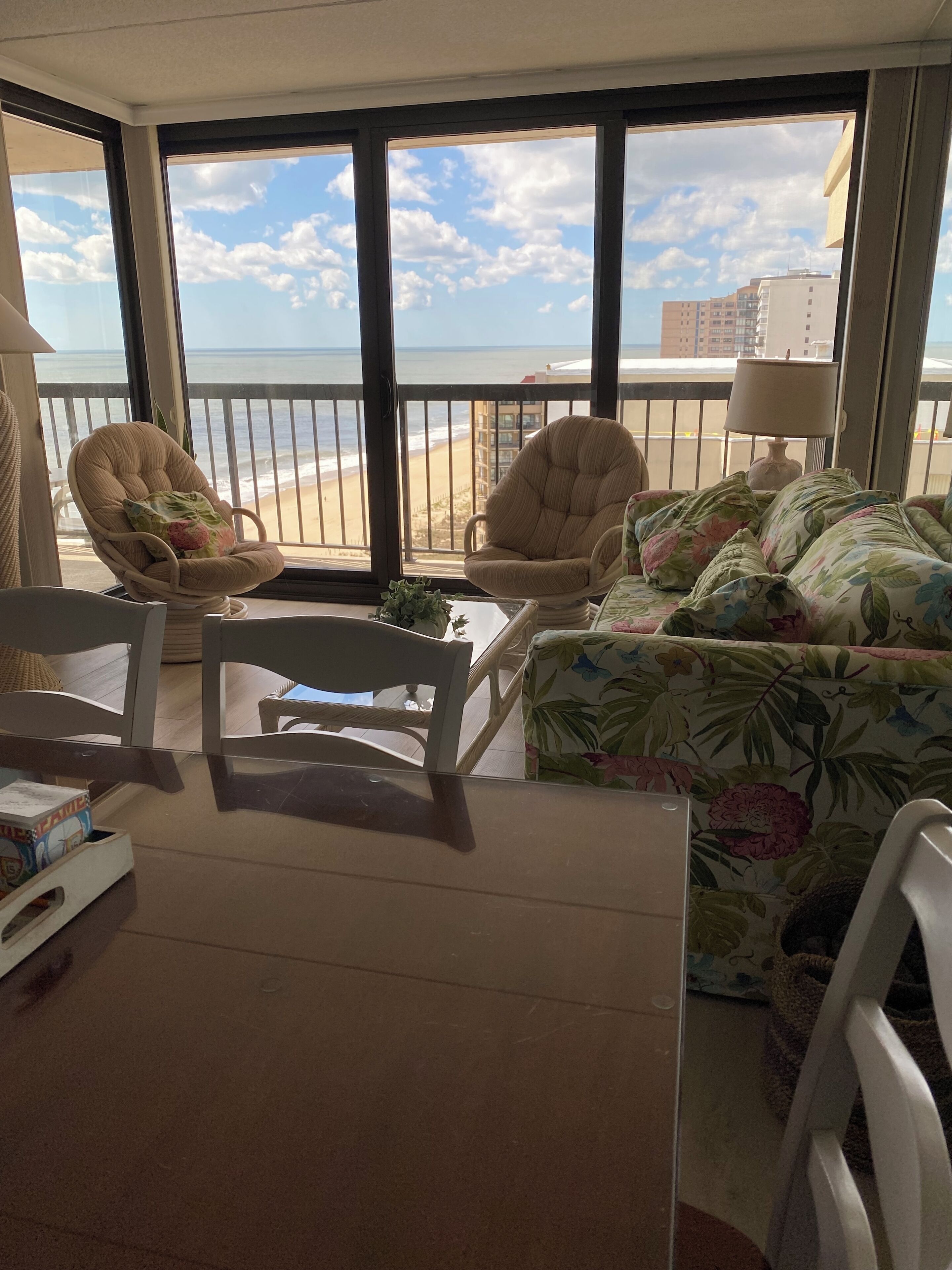 A room with a view of the beach, featuring a sofa, chairs, and a table.