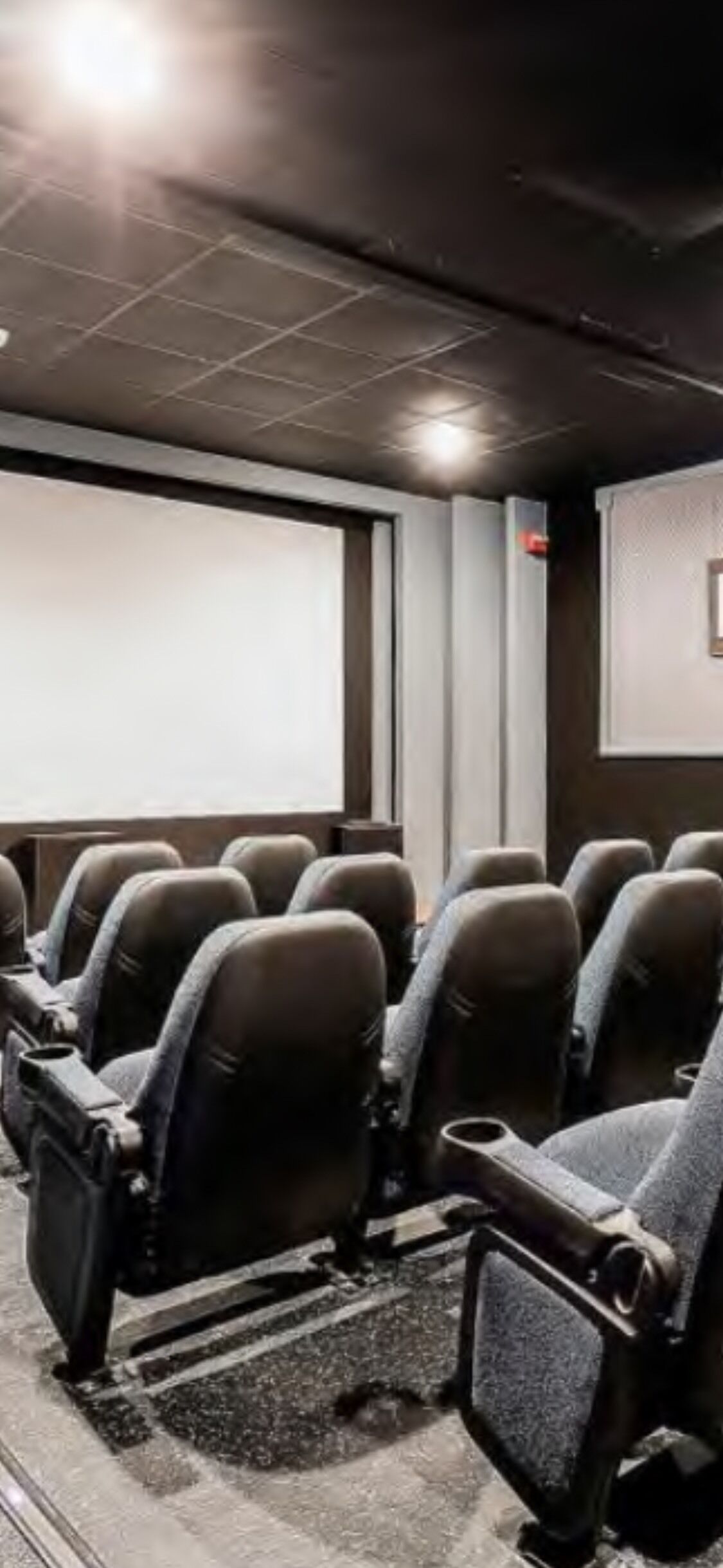 A cinema with rows of black seats, a large screen, and a dark ceiling.