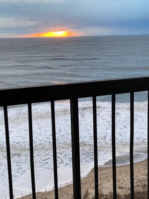 A beach view with waves, a sunset, and a wooden railing.