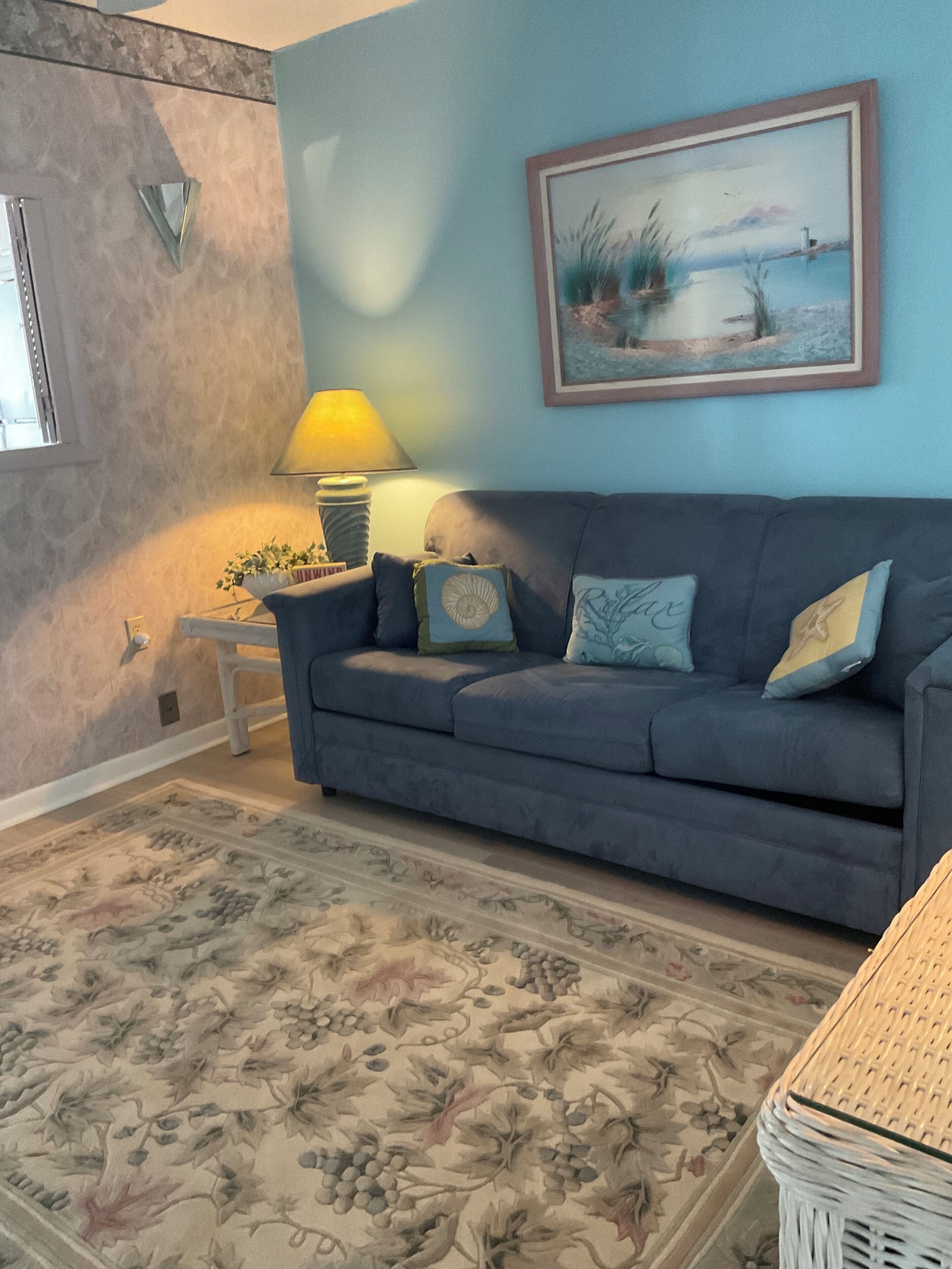 A living room with a blue sofa, a patterned rug, a lamp, and a framed painting.