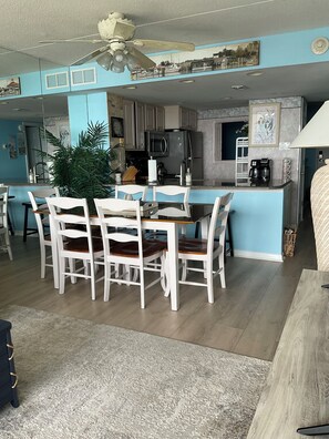 A dining area with a table and chairs, a kitchen with appliances, and a ceiling fan.