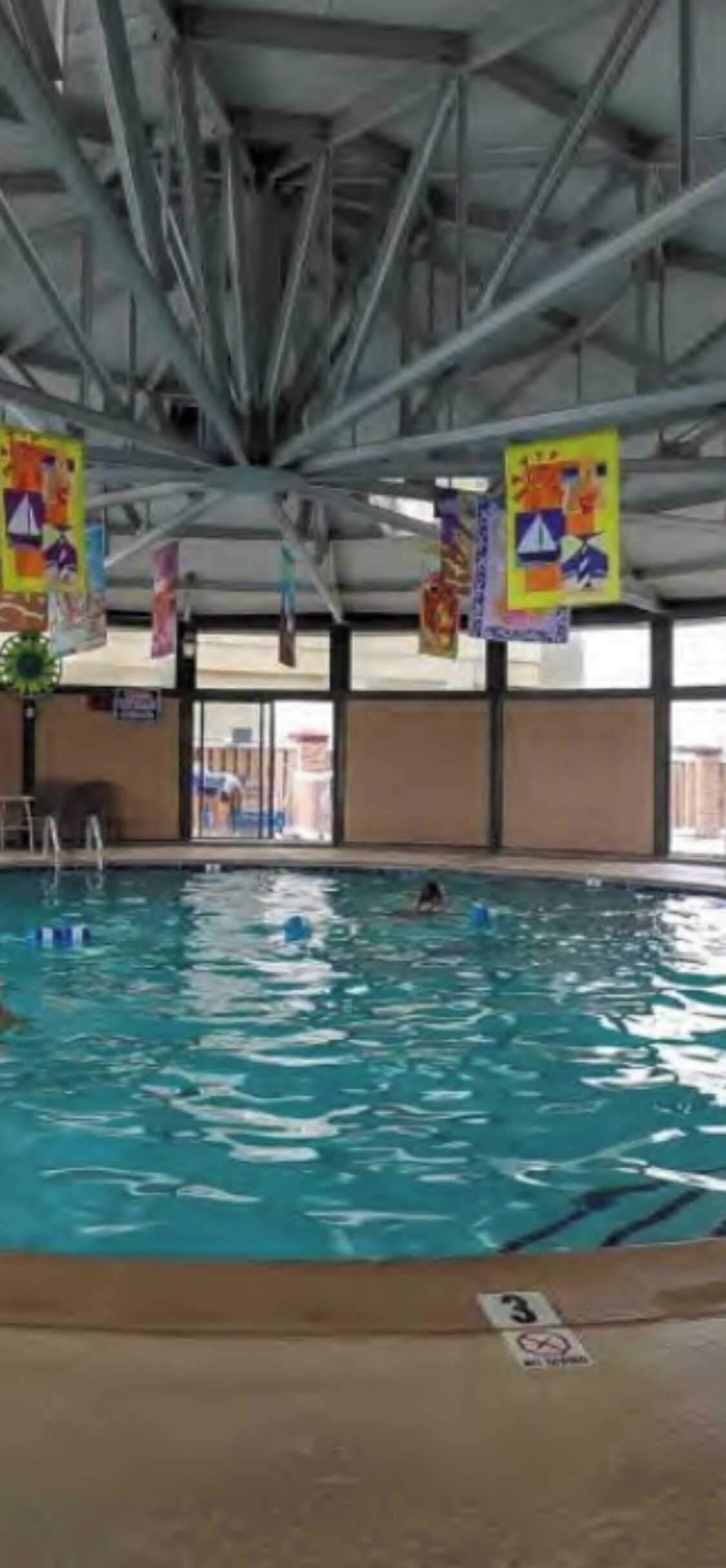 Una piscina interior con carriles delimitados, una silla de socorrista y banderines de colores.