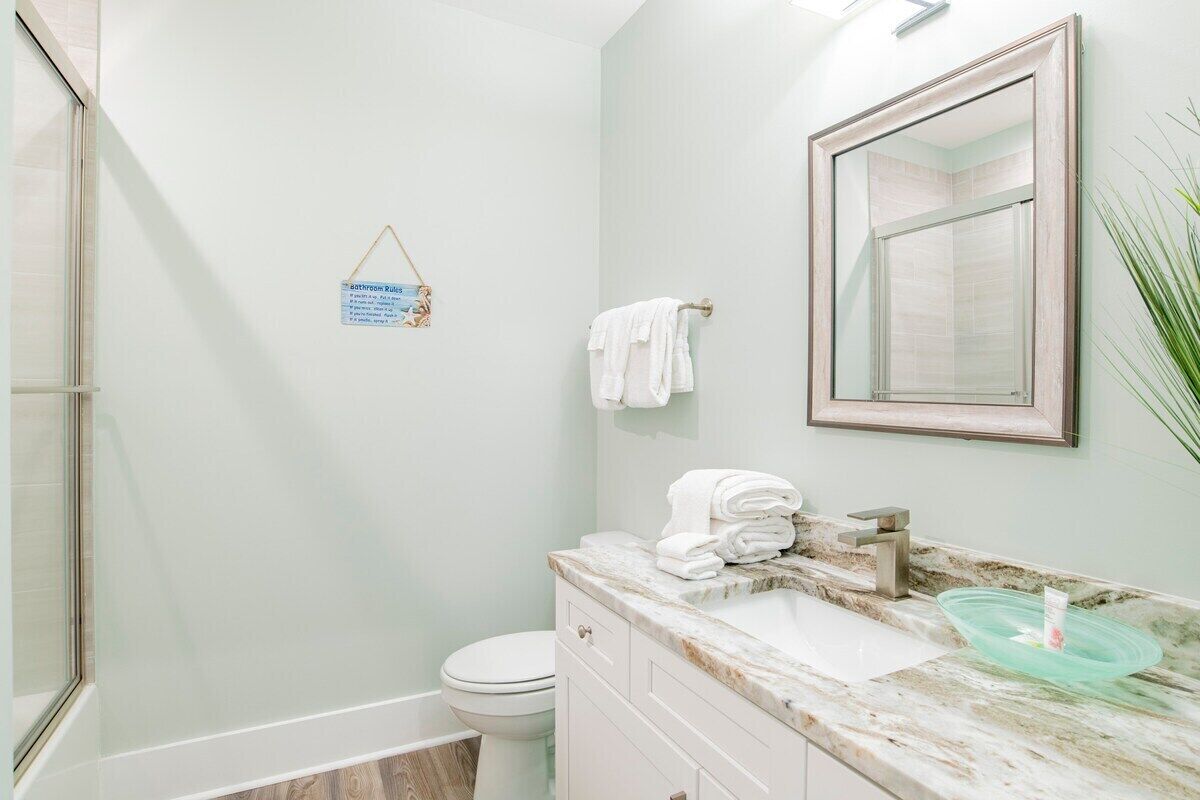 A bathroom with a toilet, sink, and shower. There is a towel rack with towels and a sign on the wall.