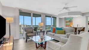A modern living room with a glass coffee table, grey sofa, and armchairs. There is a balcony with a view of the city. - Gullwing 802 (Fort Myers Beach)