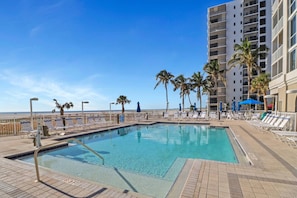 A pool area with lounge chairs and palm trees, surrounded by a high-rise building.