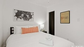 A neatly made bed with white and striped pillows, a ceiling fan, a framed poster on the wall, and a small nightstand with a lamp. - Brookswood #A xxxxxx (Austin)